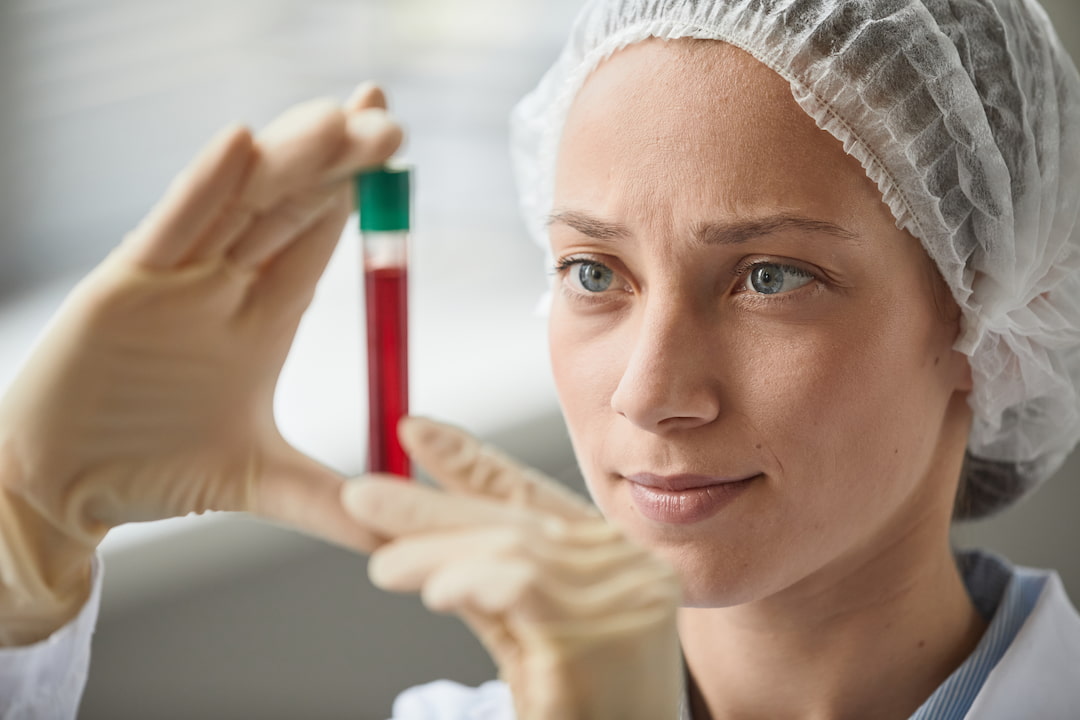 a woman in a lab suit looking at a tube filled with red fluid