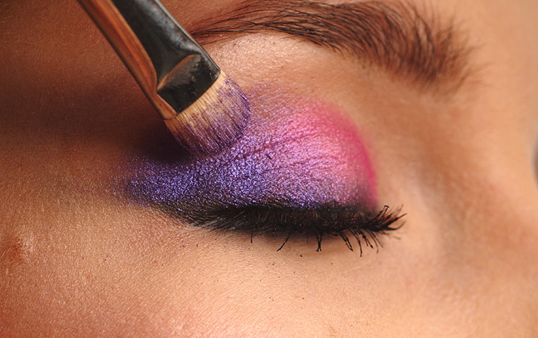 closeup picture of a woman's eyelid being applied a makeup
