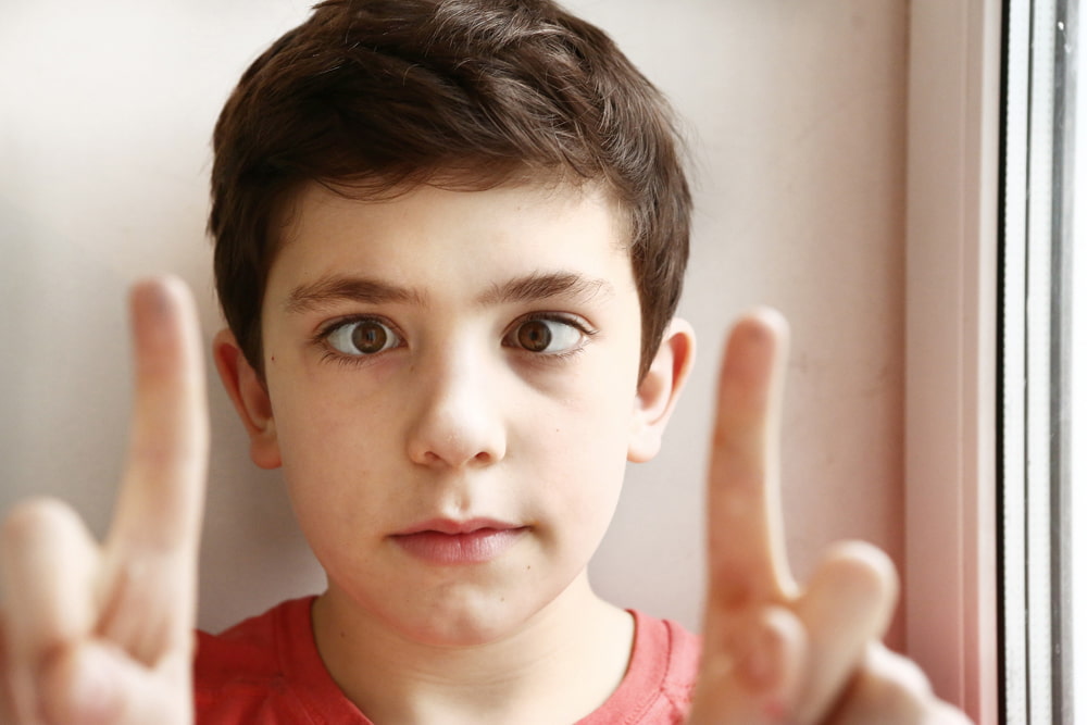 a child posing with both of his index fingers in front of his face, squinting his eyes.